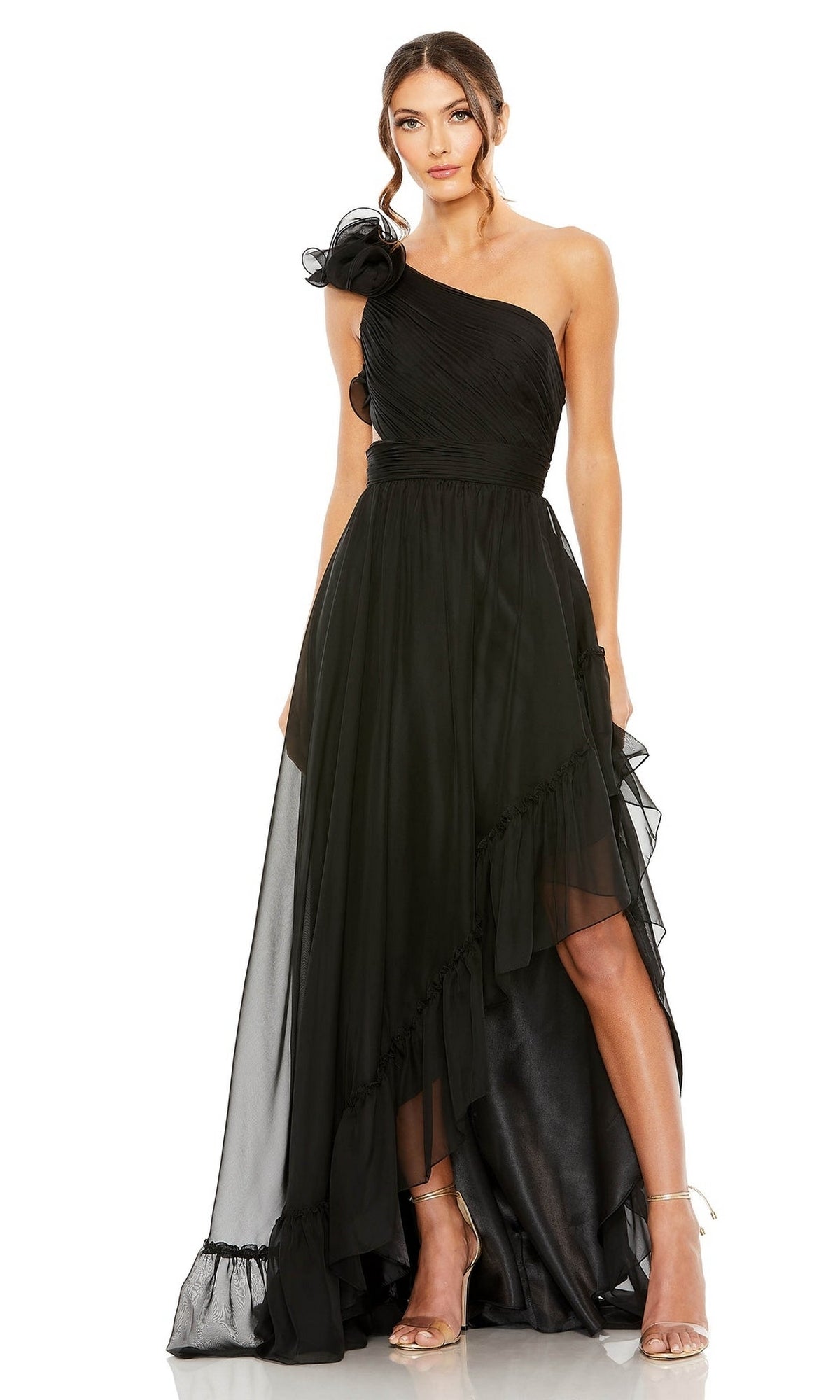A woman in the Long Formal Dress 67989 by Mac Duggal, featuring a one-shoulder design, asymmetrical hem, floral shoulder detail, and strappy heels, stands against a white background showcasing modern elegance.